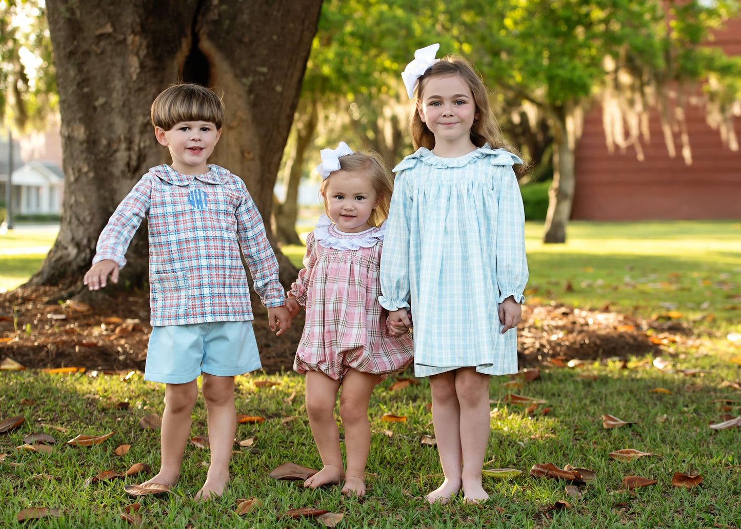 Three children standing together in a park with trees and grass in the background