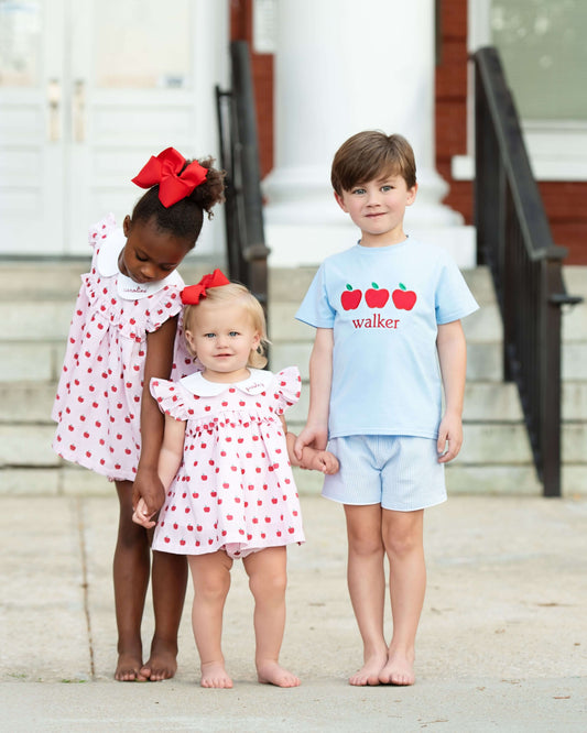 Three children standing together outdoors, wearing matching outfits with red polka dots.