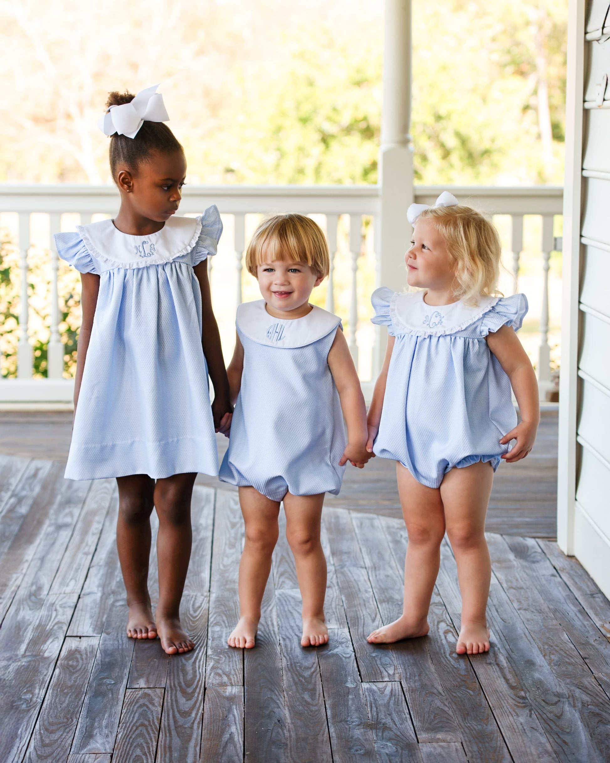 Three children wearing matching light blue outfits, standing on a wooden deck.