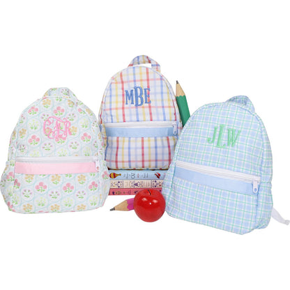 Three colorful backpacks with monogramming and stationery items on a white background