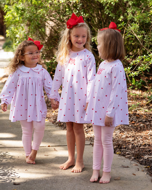 Three young girls in matching outfits with red bows outdoors.