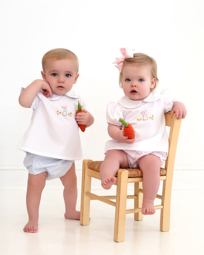Two babies in matching outfits holding toy carrots on a white background