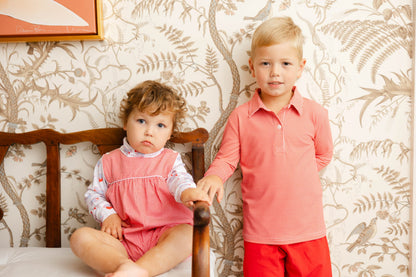 Two children, a boy and a girl, standing in front of a floral wallpapered wall.