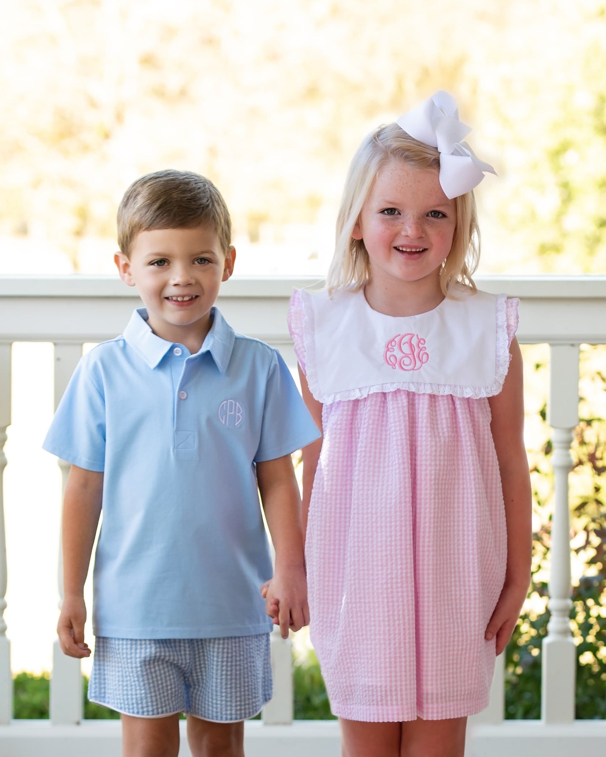 Two children, a boy and a girl, standing on a porch with a blurred outdoor background.