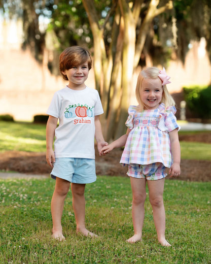 Two children holding hands in a park with trees and grass in the background.