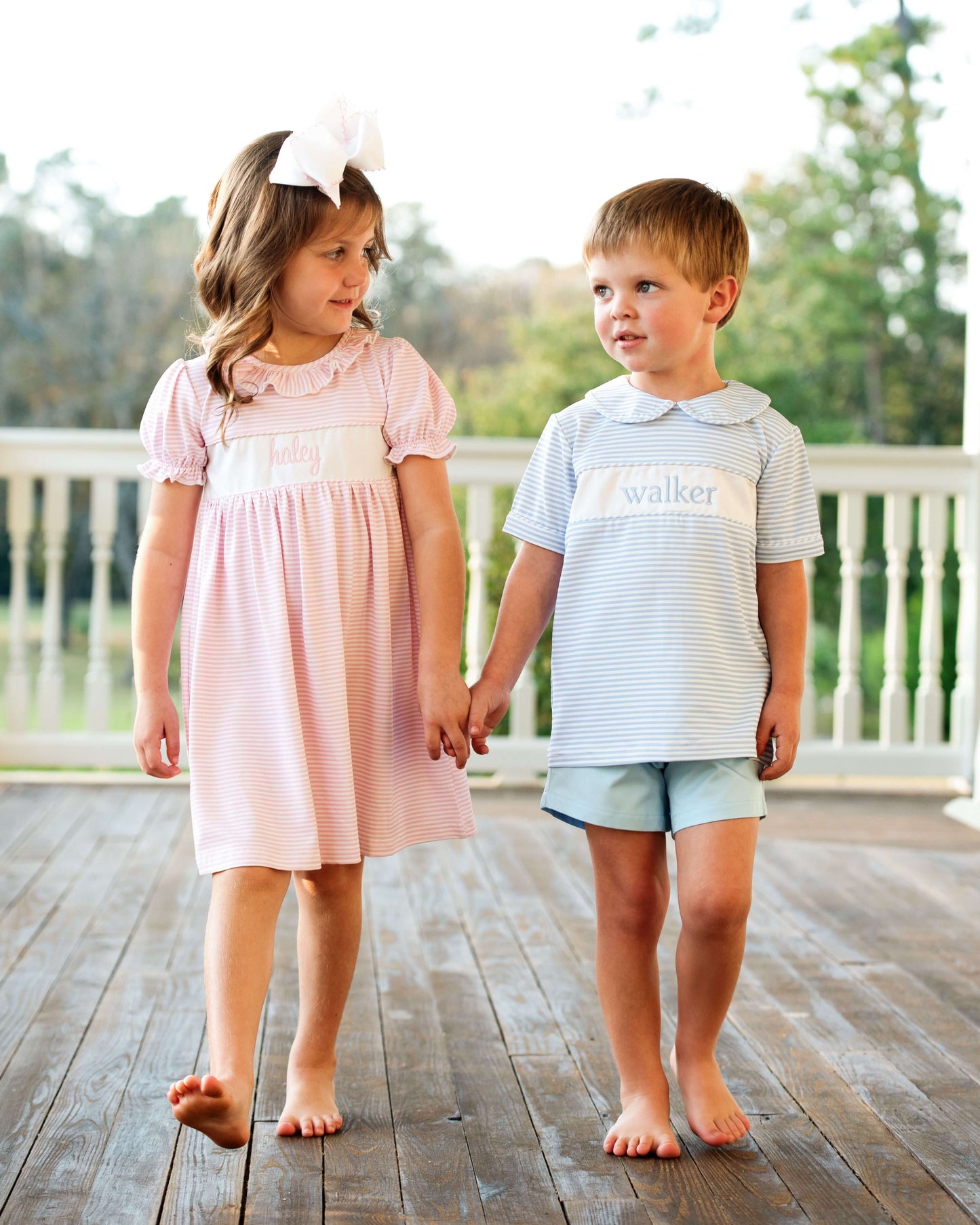Two children holding hands on a wooden deck with a blurred natural background