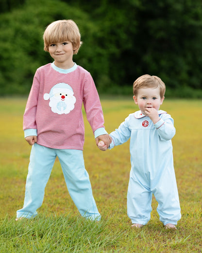 Two children holding hands outdoors, one wearing a pink sweater with a white dog design and the other in a light blue onesie.