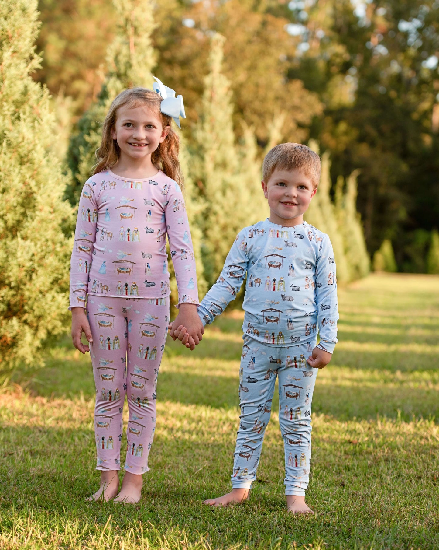 Two children holding hands outdoors wearing pajamas with vehicle patterns.