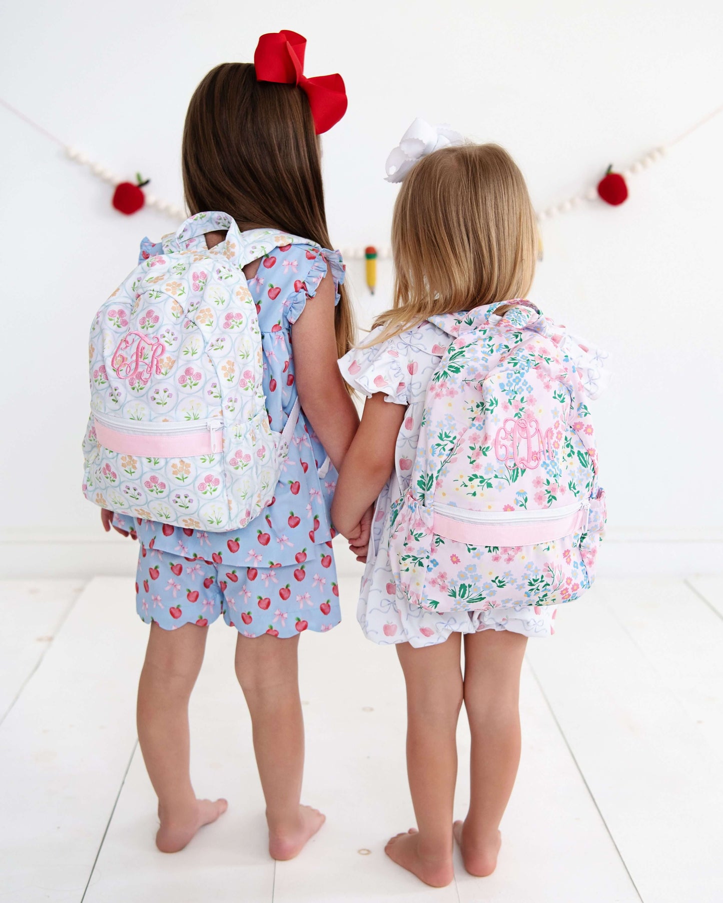 Two children holding hands with backpacks on. 