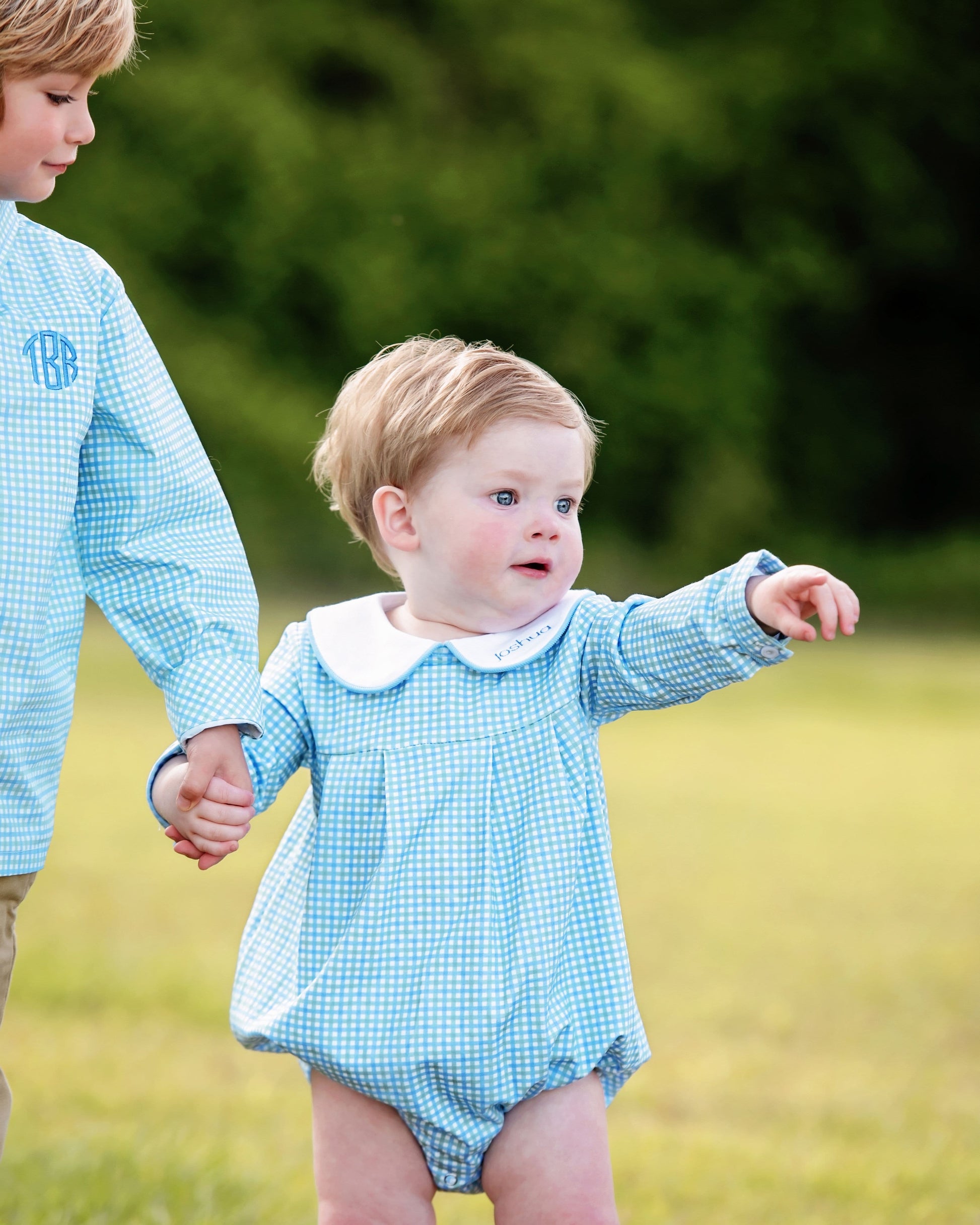 Two children in matching blue checkered outfits standing outdoors.