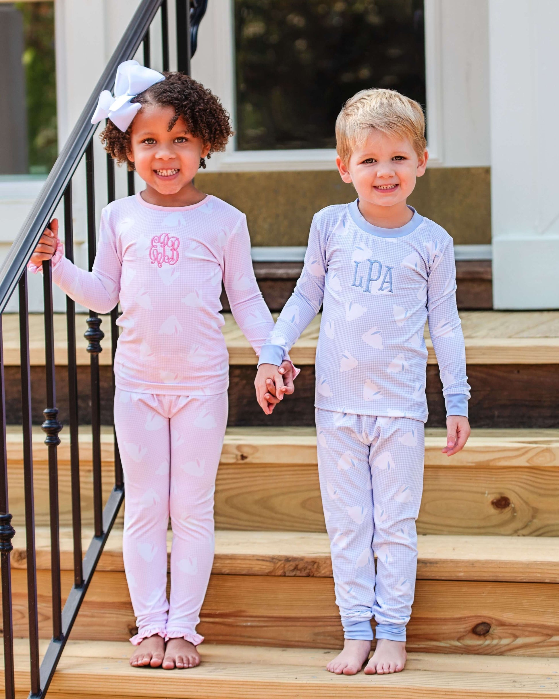 Two children in matching pajamas standing on wooden steps.