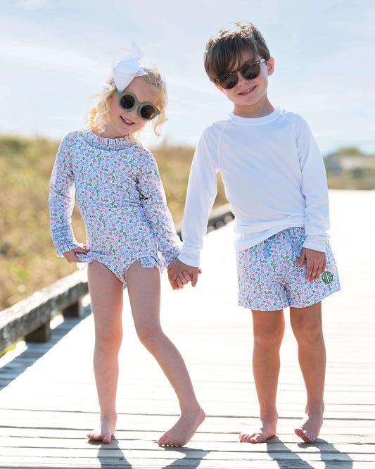Two children in matching floral outfits standing on a wooden boardwalk.