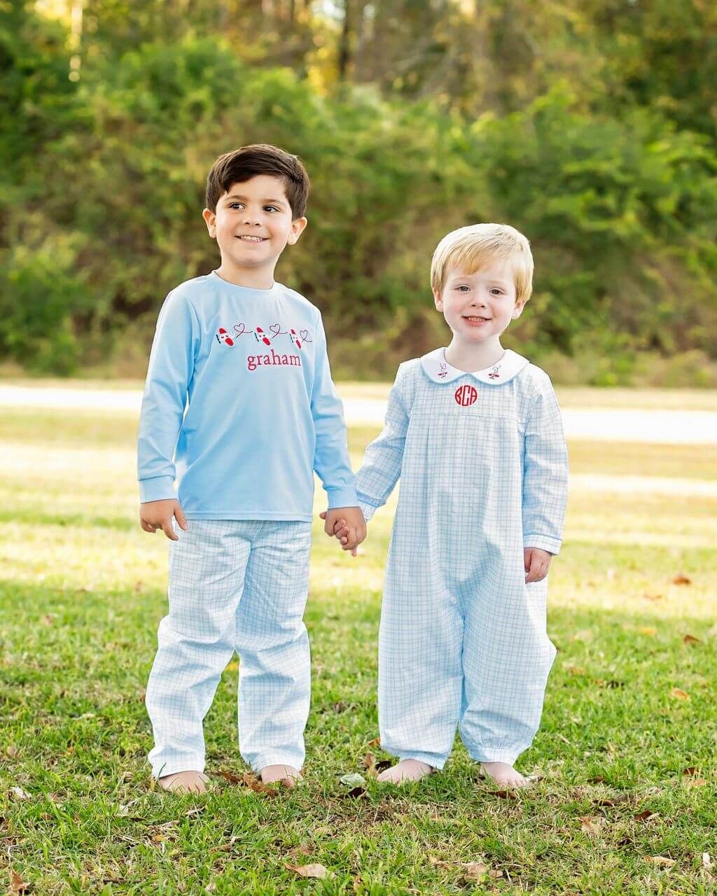 Two children in matching light blue outfits standing outdoors on grass with trees in the background.