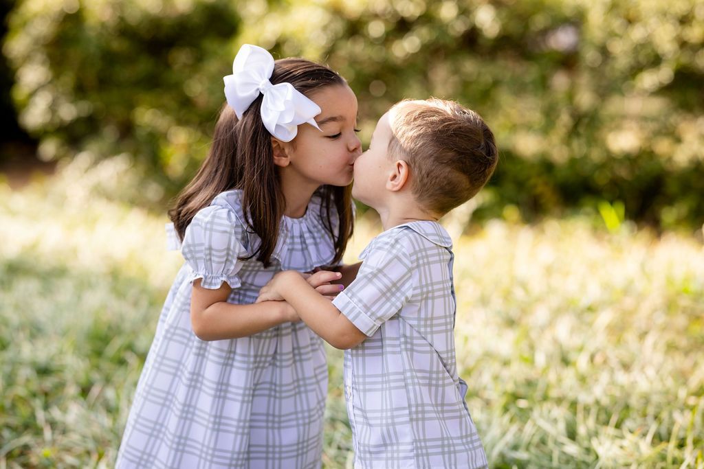 Two children in matching outfits kissing in a grassy field.