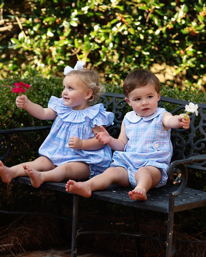 Two children in matching outfits sitting on a bench outdoors.