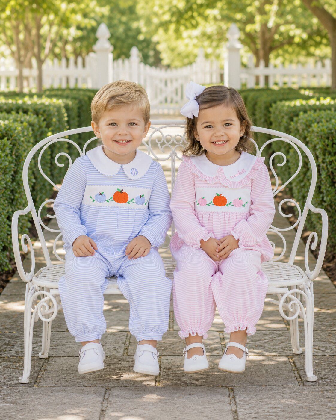 Two children in matching outfits sitting on a white bench outdoors.
