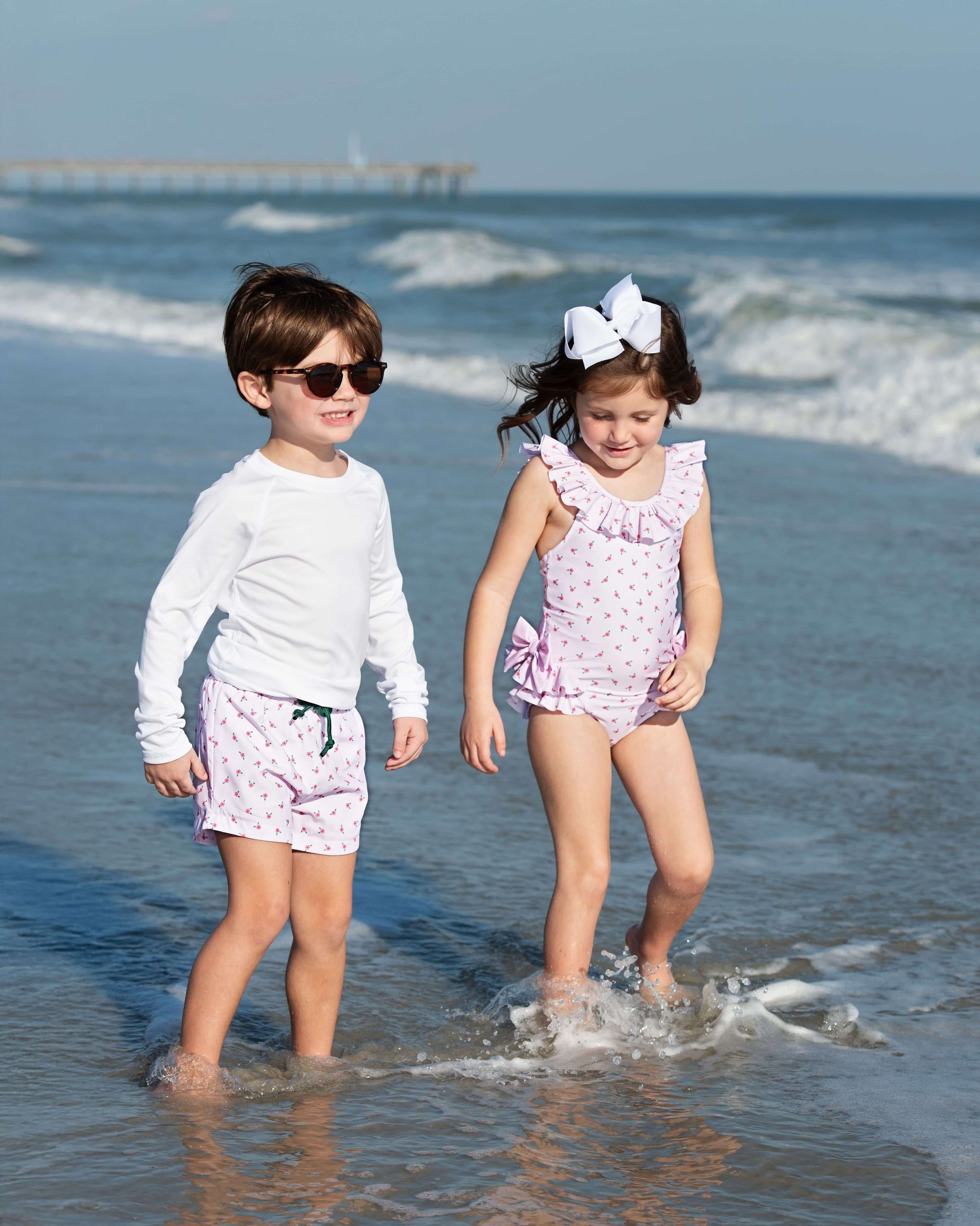 Two children in matching outfits standing in shallow water at the beach.