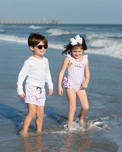 Two children in matching outfits standing in shallow water at the beach.