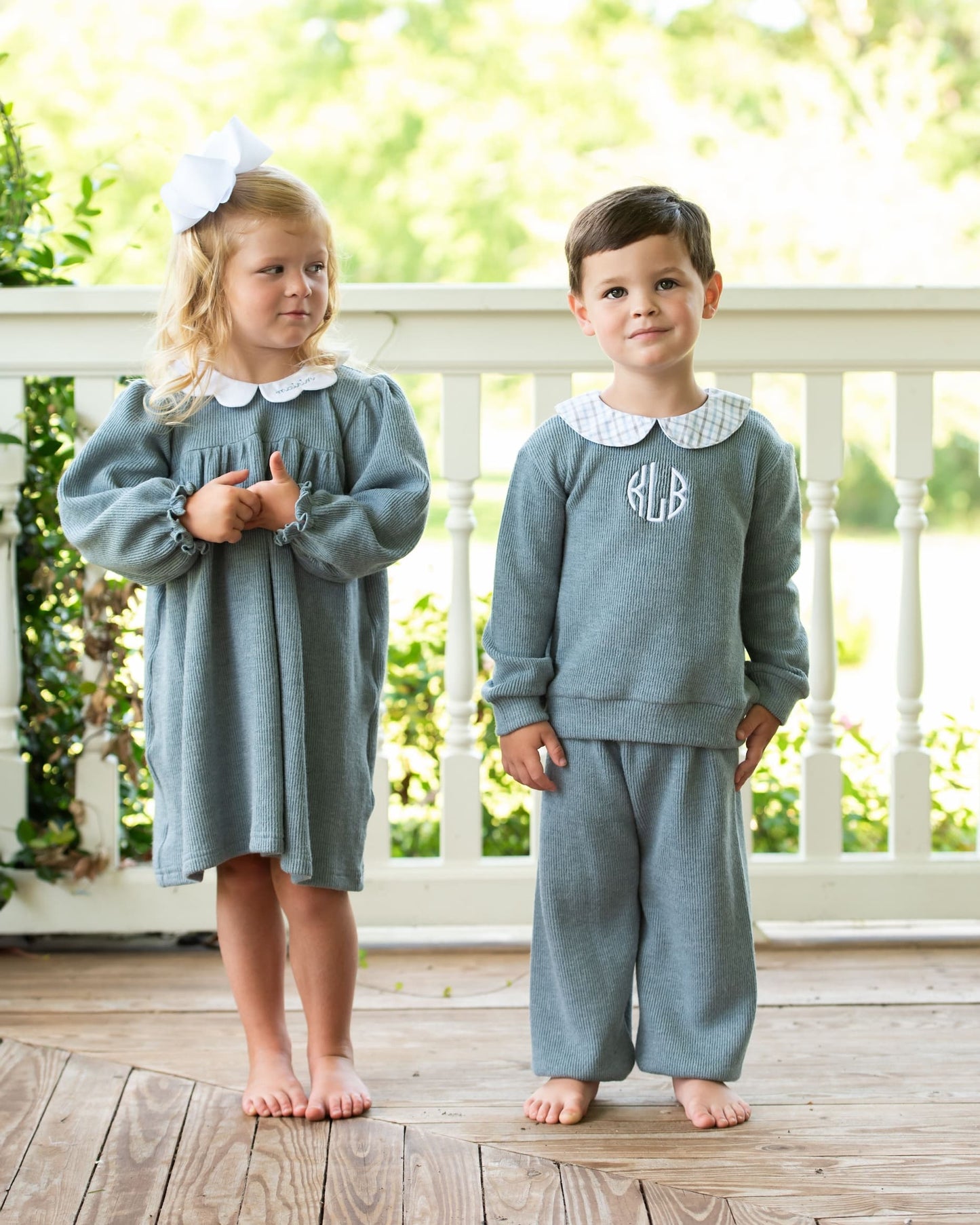 Two children in matching outfits standing on a wooden deck.