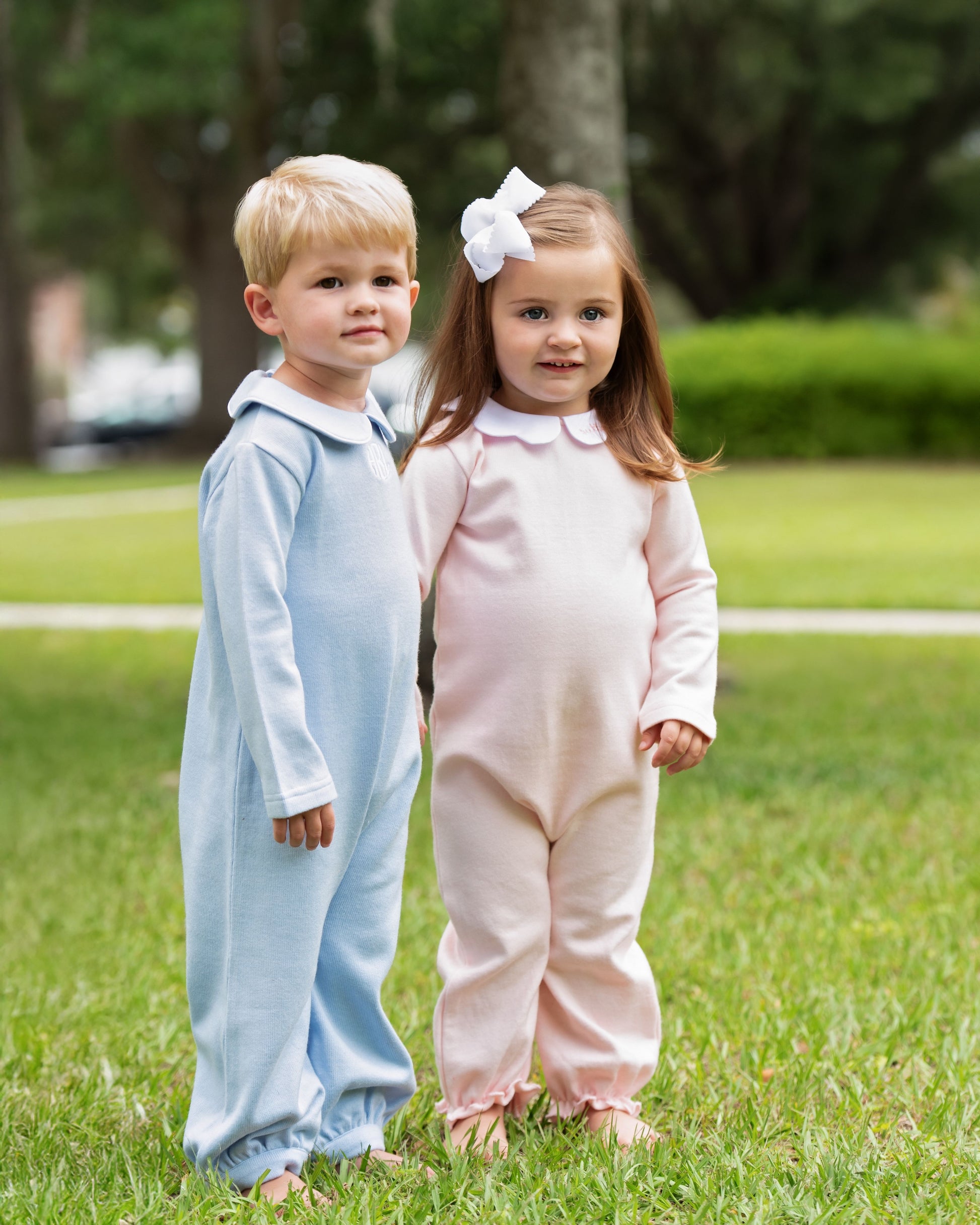 Two children in matching outfits standing on grass with trees in the background