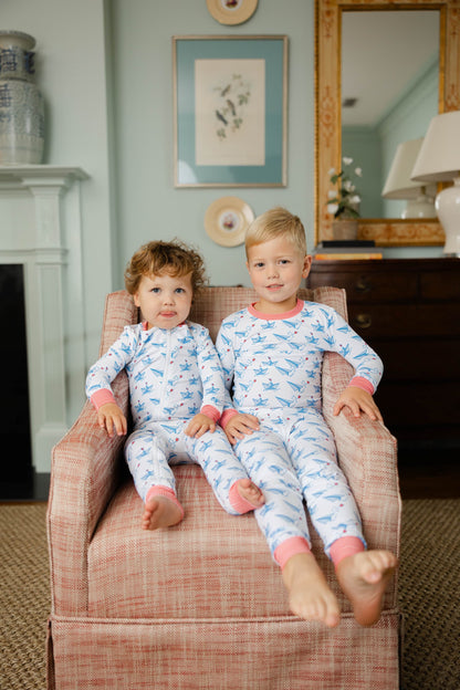 Two children in matching pajamas sitting on a plaid chair in a room with a fireplace and framed pictures.