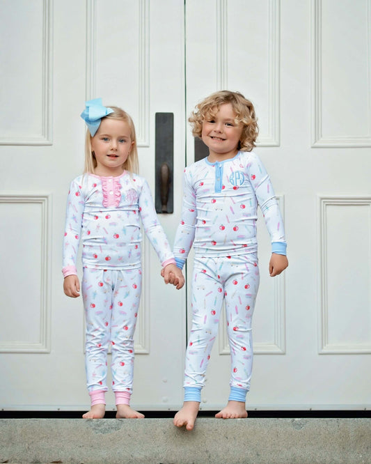 Two children in matching pajamas standing in front of a white door.