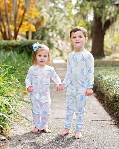 Two children in matching pajamas standing on a path with trees and grass in the background.