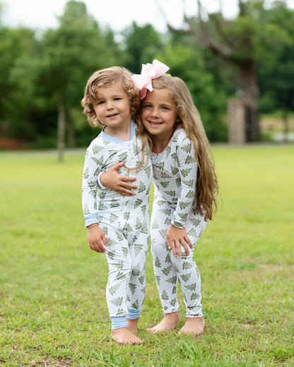 Two children in matching pajamas standing on grass with trees in the background