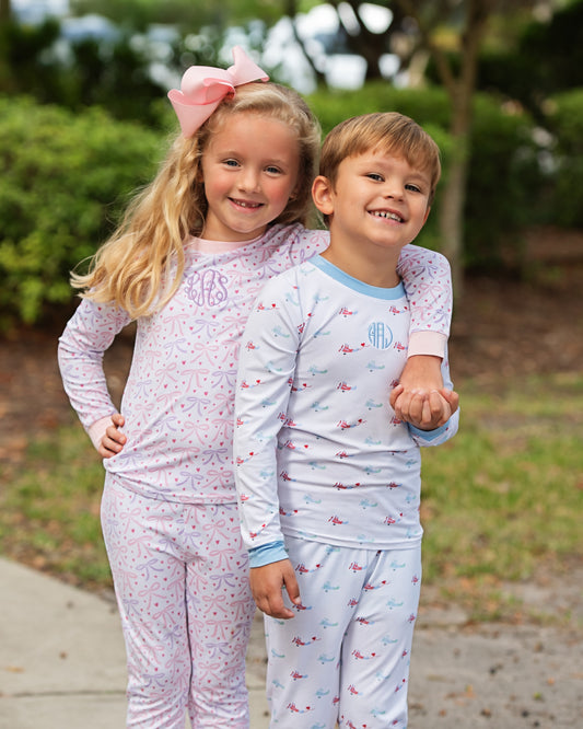 Two children in matching pajamas standing outdoors with a blurred background