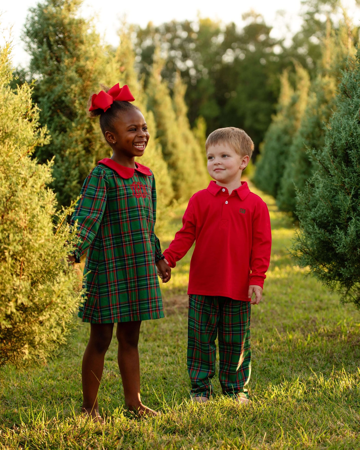 Two children in matching plaid outfits standing in a field with trees.