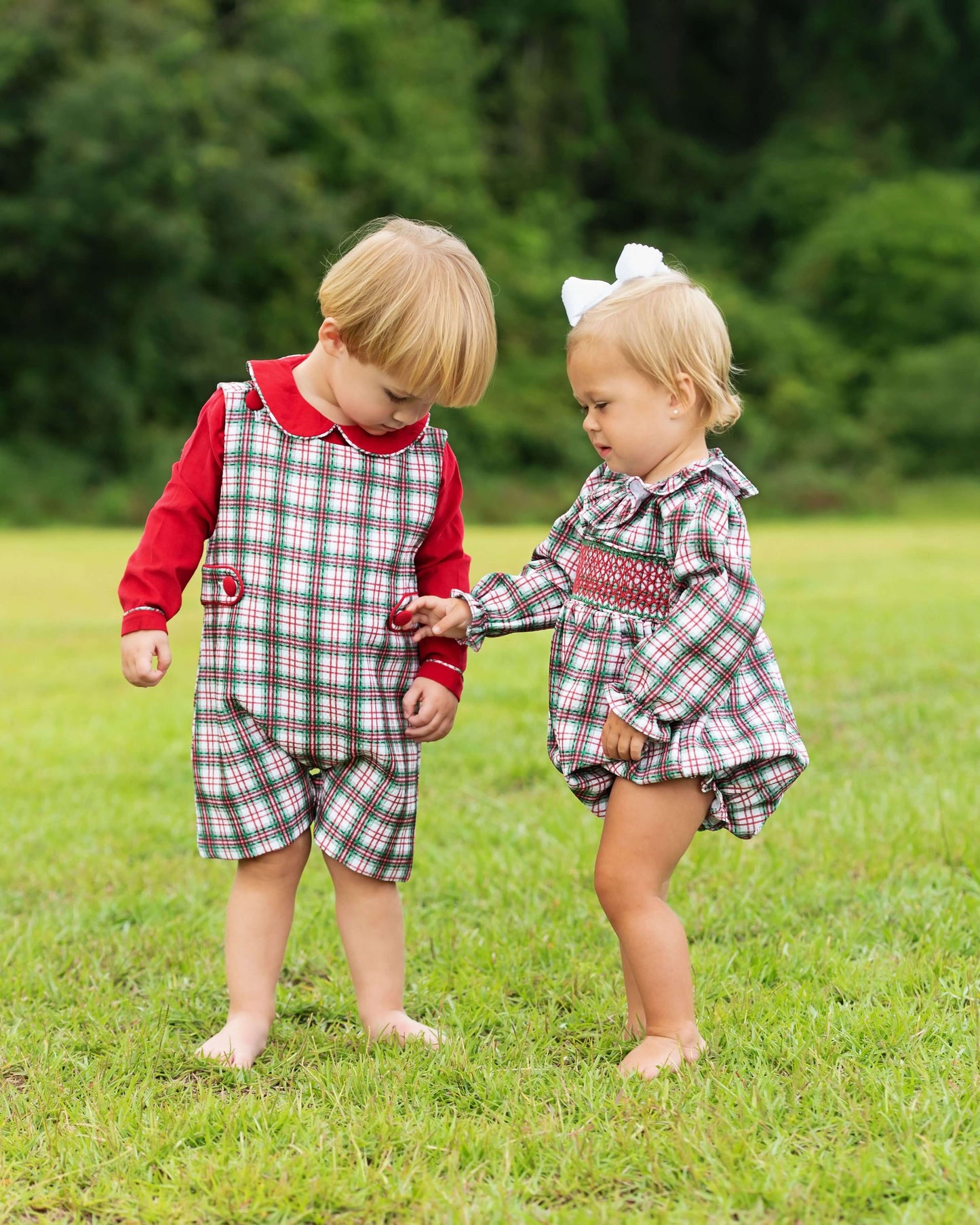 Two children in matching plaid outfits standing on grass with a blurred green background