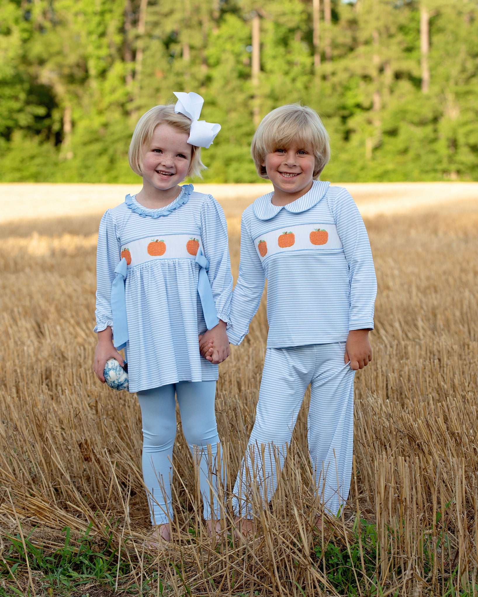 Two children in matching pumpkin  outfits standing in a field with trees in the background
