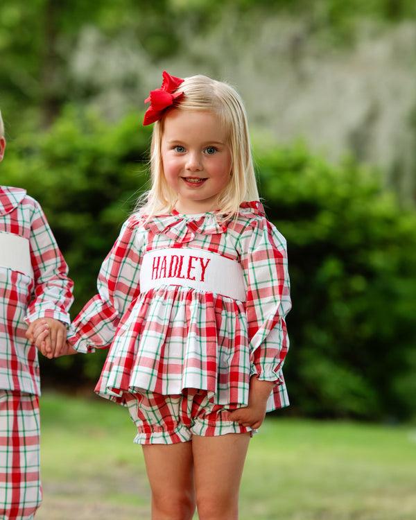 Two children in matching red and green plaid custom smocked outfits outdoors