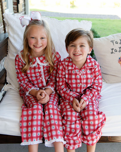 Two children in matching red plaid outfits sitting on a couch.