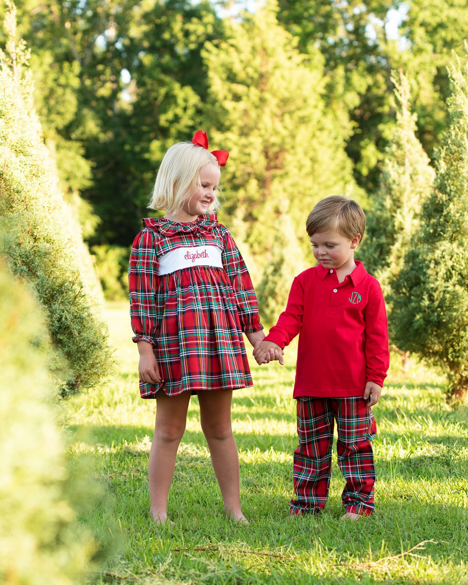 Two children in matching red plaid outfits standing in a field with trees in the background.