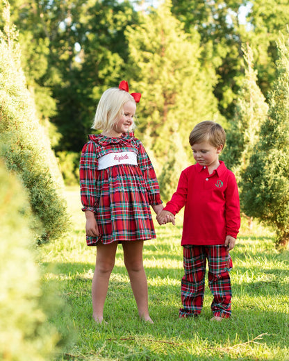 Two children in matching red plaid outfits standing in a field with trees in the background.