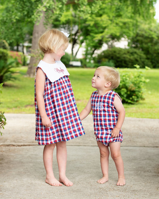 Two children in matching red, white, and blue outfits standing outdoors on a path.