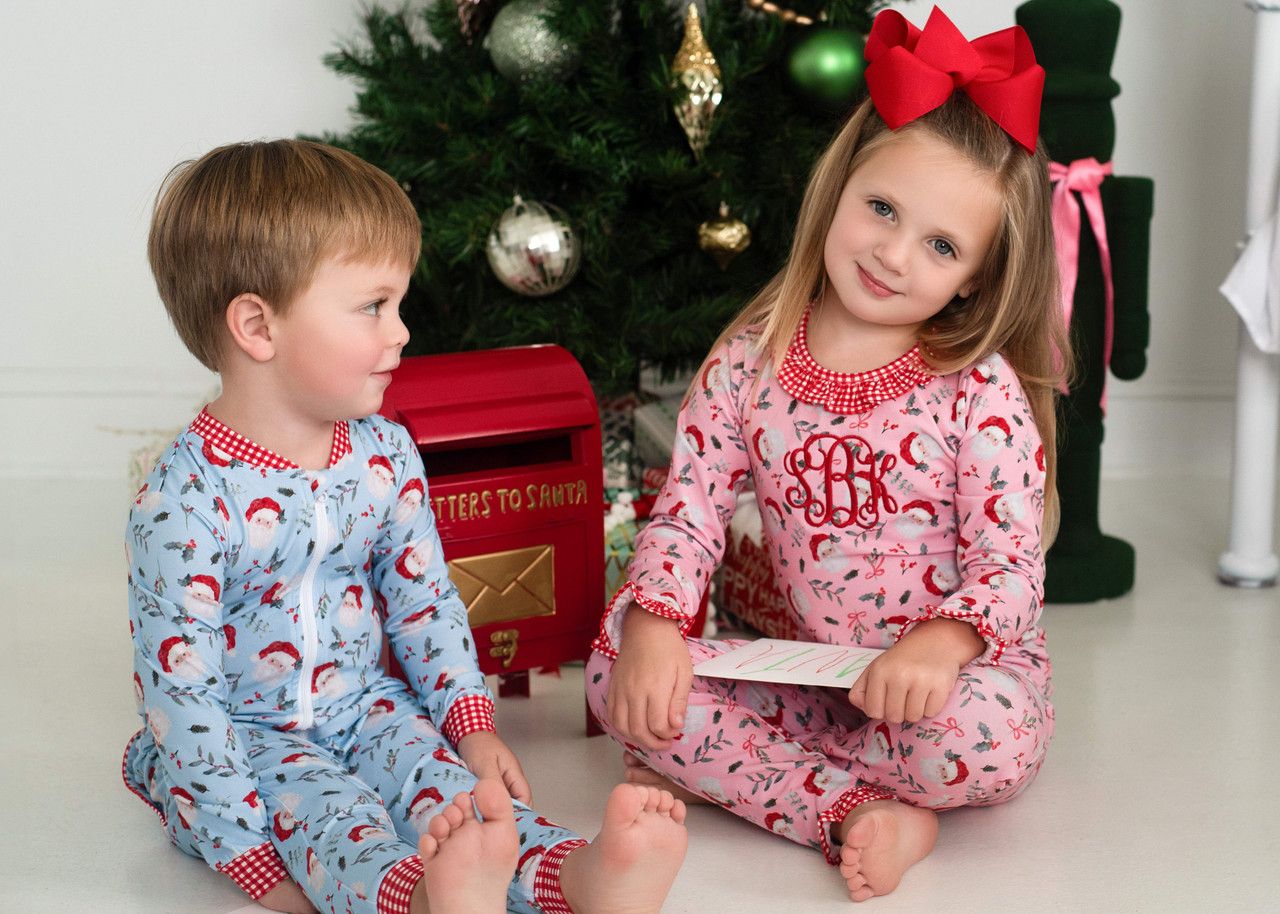 Two children in pajamas sitting on the floor in front of a Christmas tree.