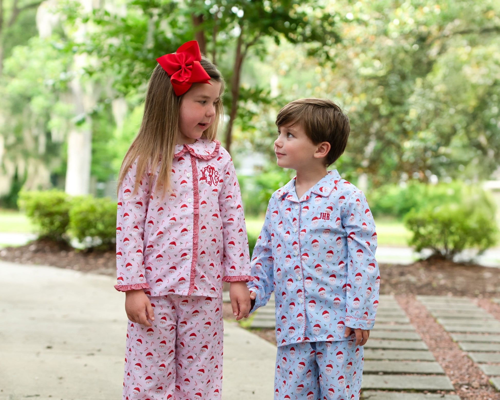 Two children in pajamas standing outdoors with greenery in the background