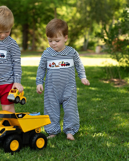 Two children playing with toy trucks in a grassy outdoor area.