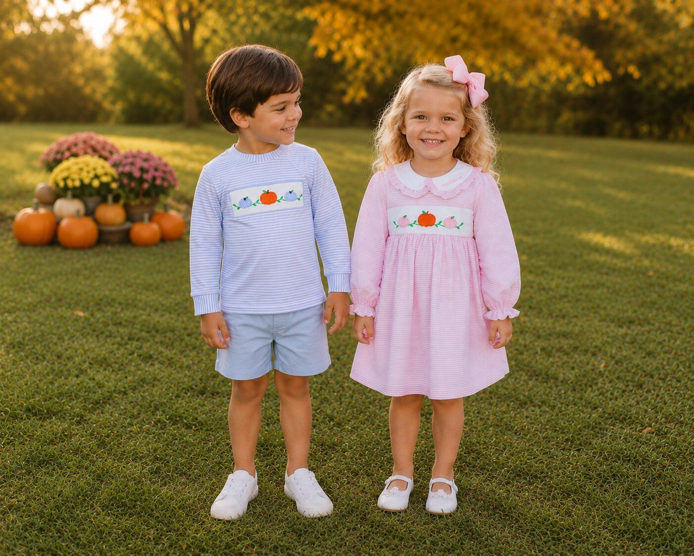 Two children, standing in a grassy field with pumpkins and flowers in the background.