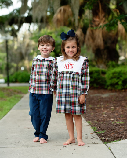 Two children standing on a sidewalk outdoors, wearing matching plaid outfits. 