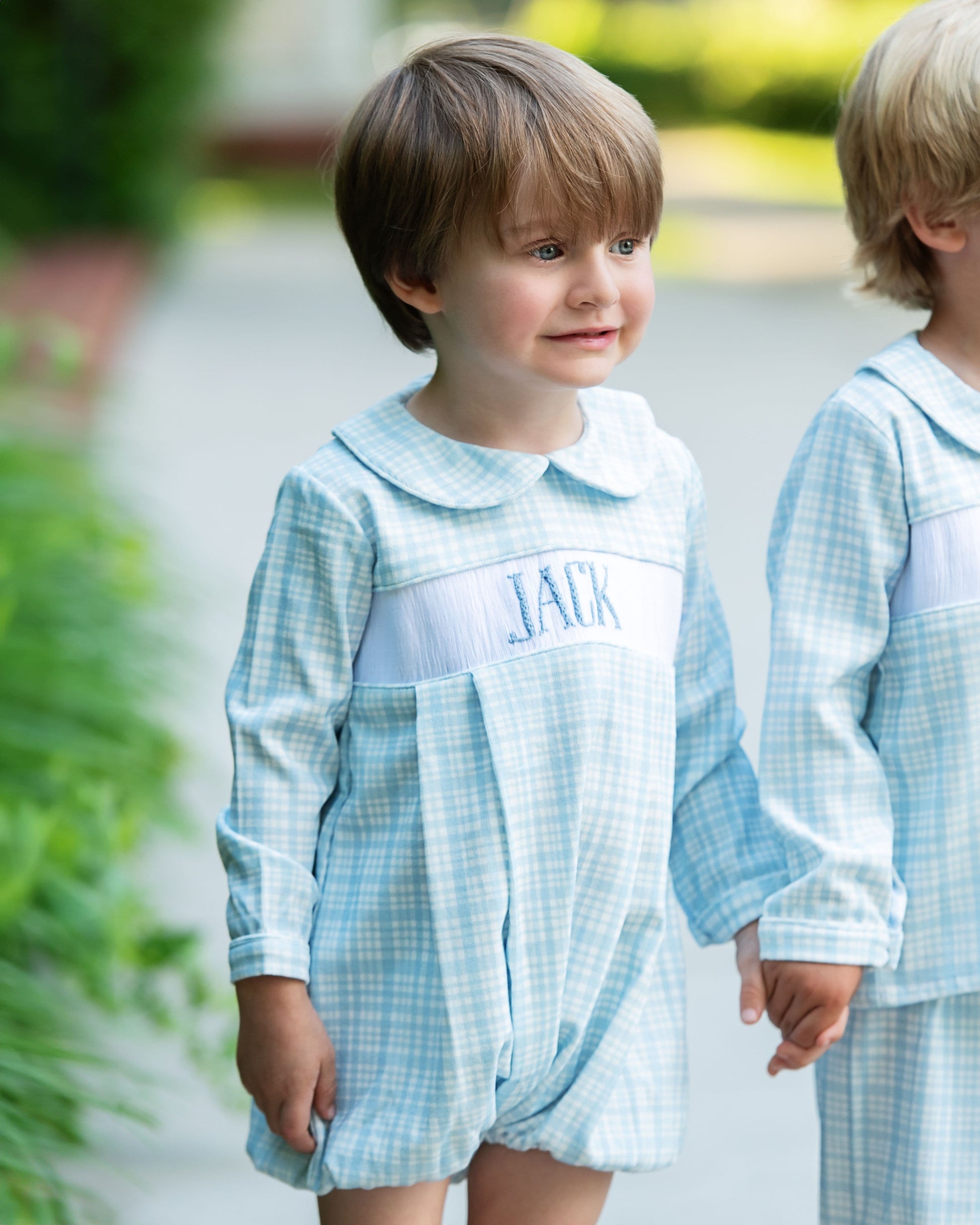 Two children wearing matching blue checkered outfits outdoors.