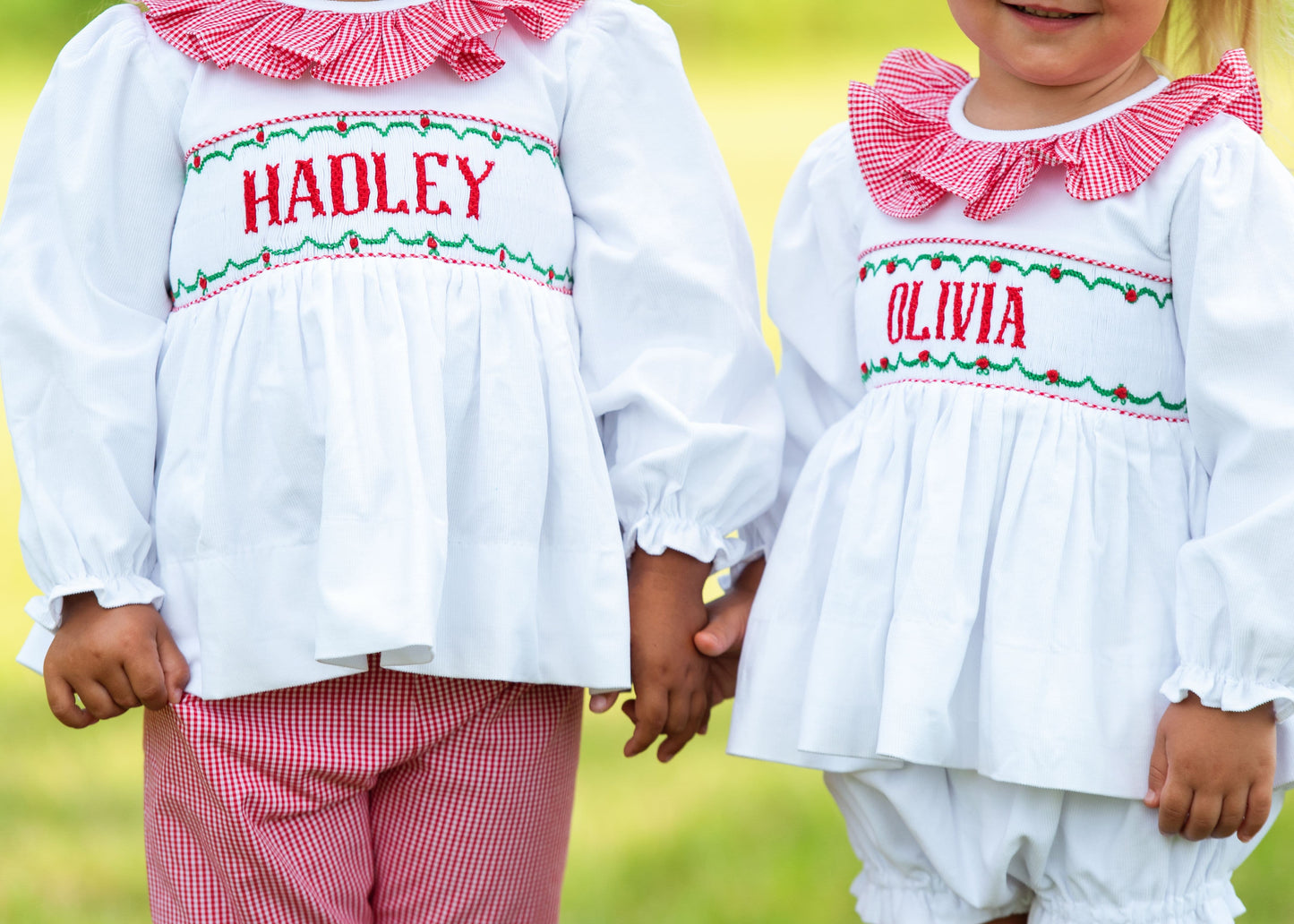 Two children wearing matching outfits with embroidered names against a blurred green background