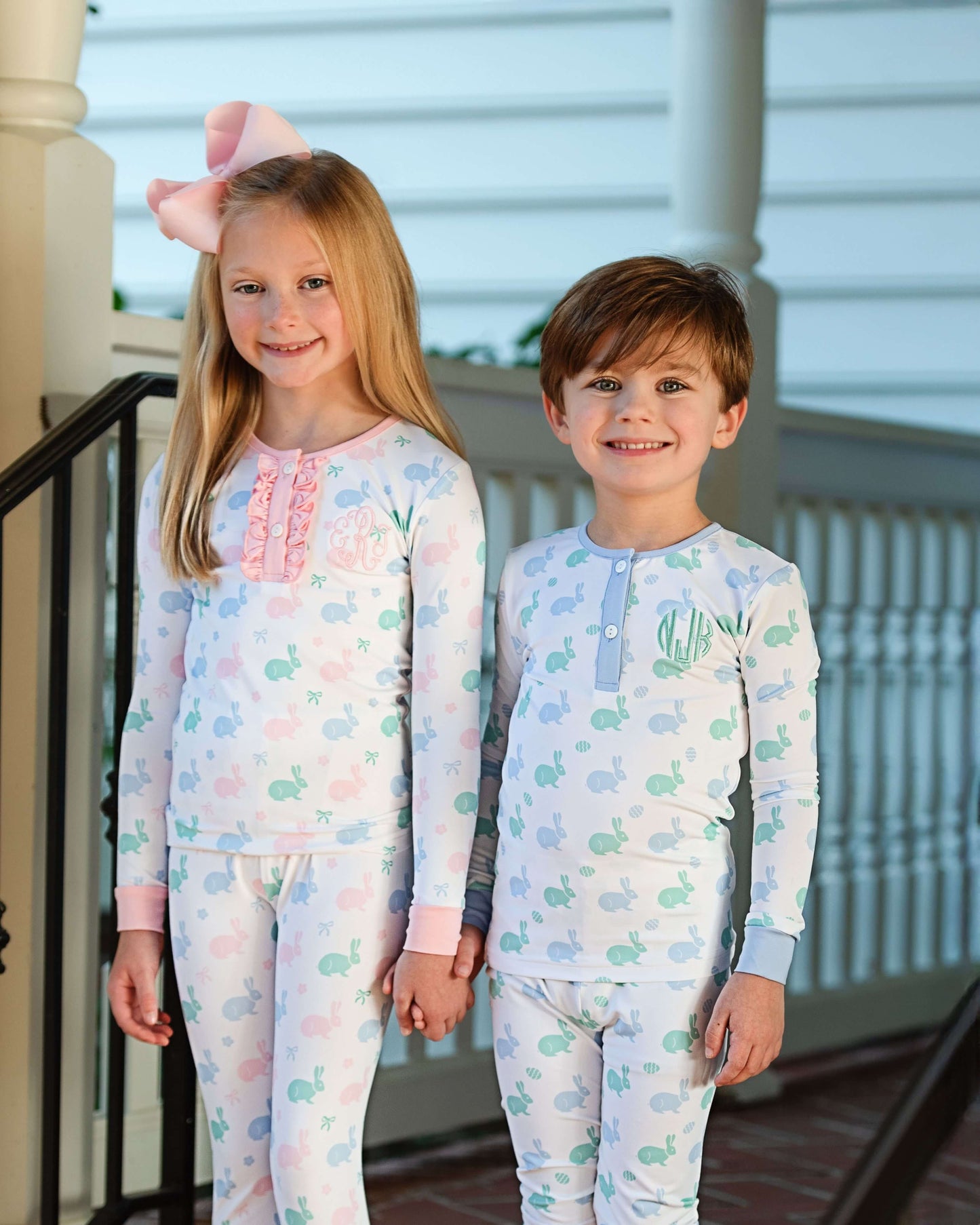 Two children wearing matching pajamas standing on a porch.
