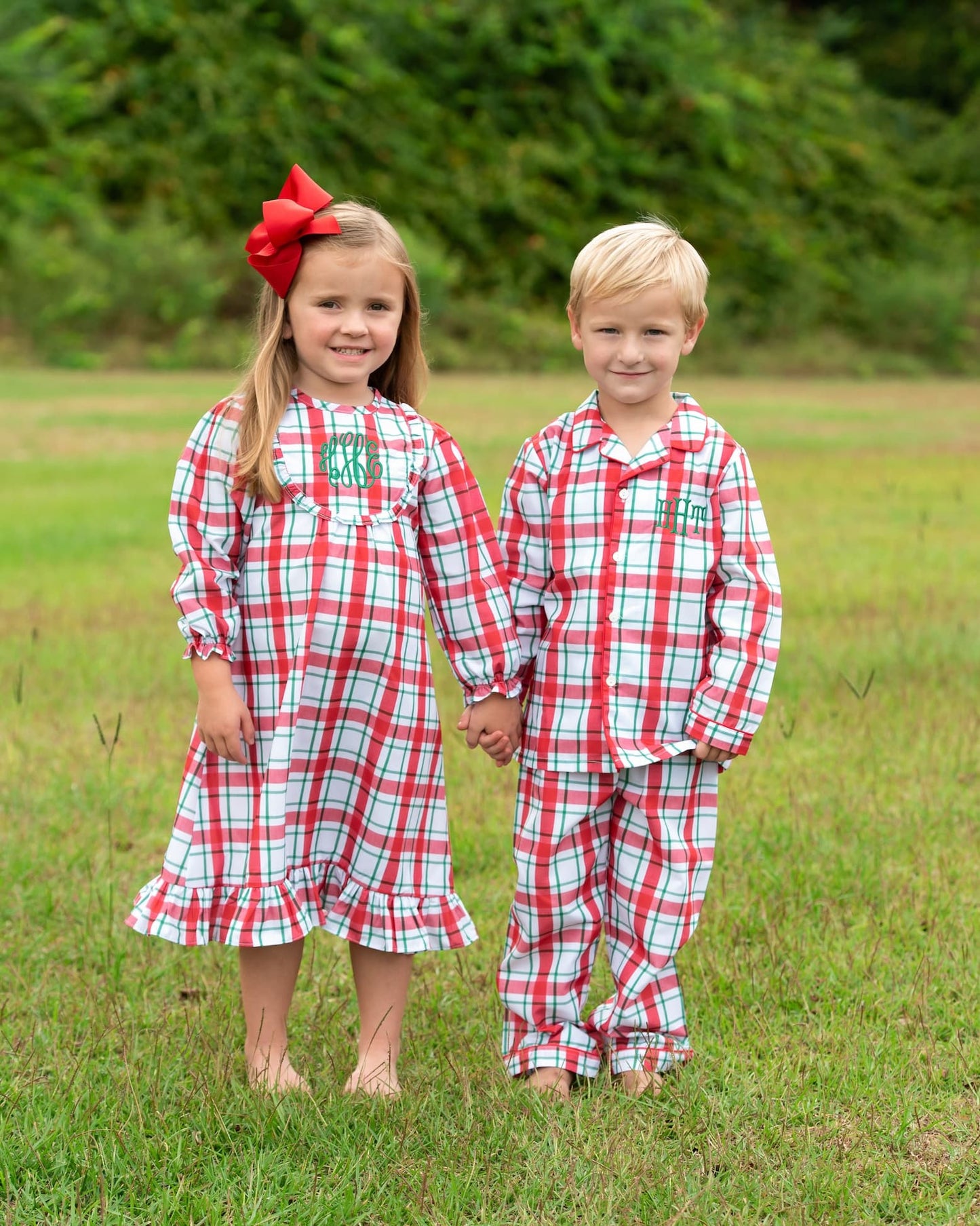 Two children wearing matching red and green plaid pajamas standing in a grassy field.