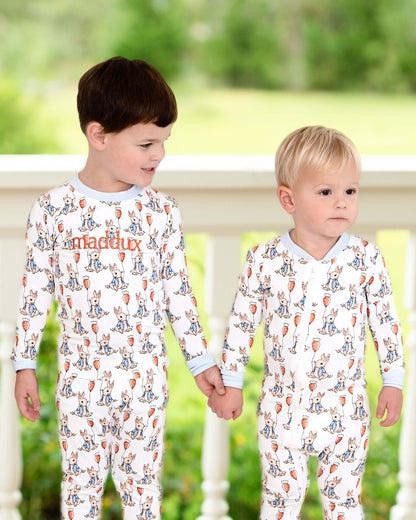 Two children wearing pajamas with a pattern of animals and text, standing on a wooden deck.