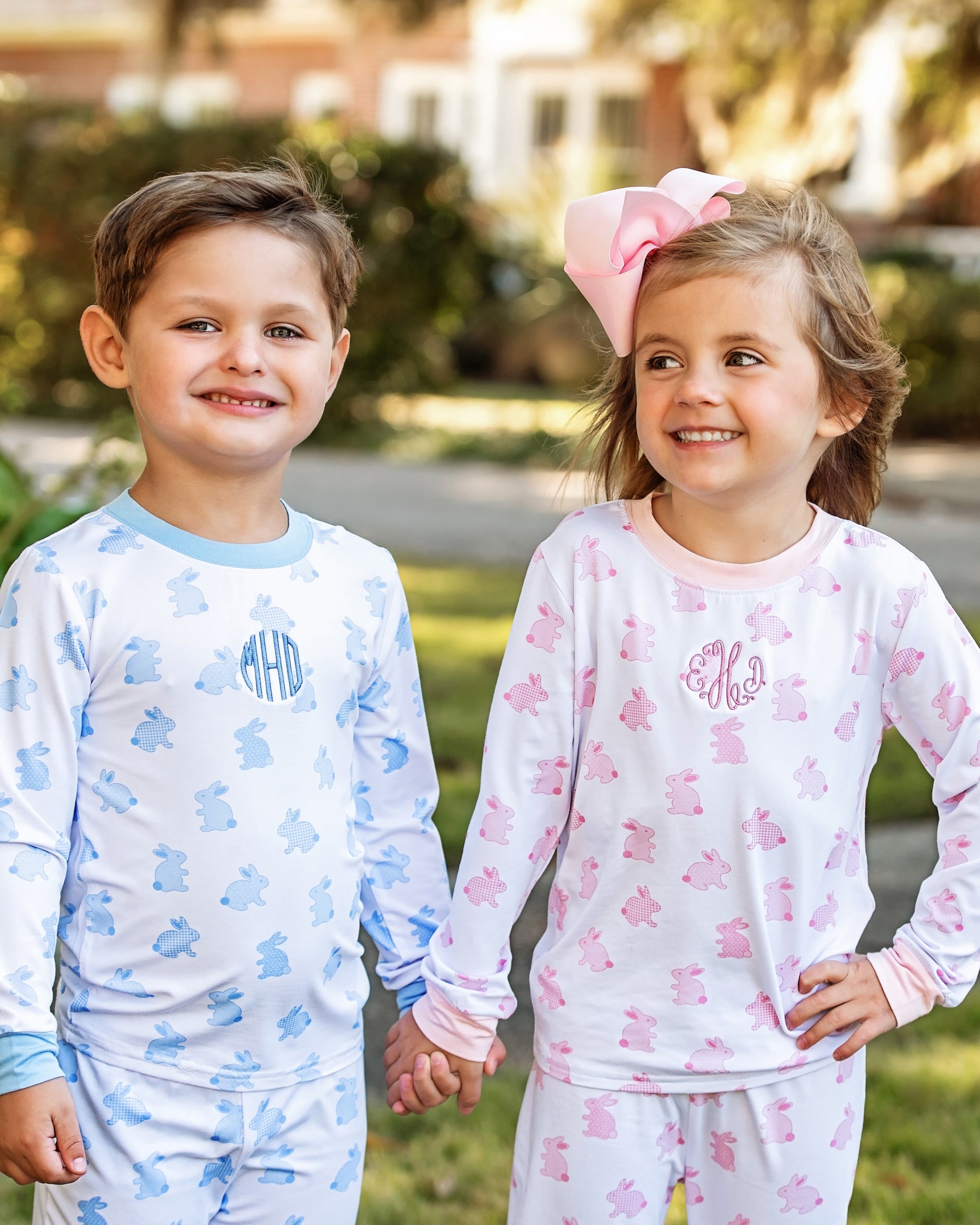 Two children wearing pajamas with monograms, standing outdoors.