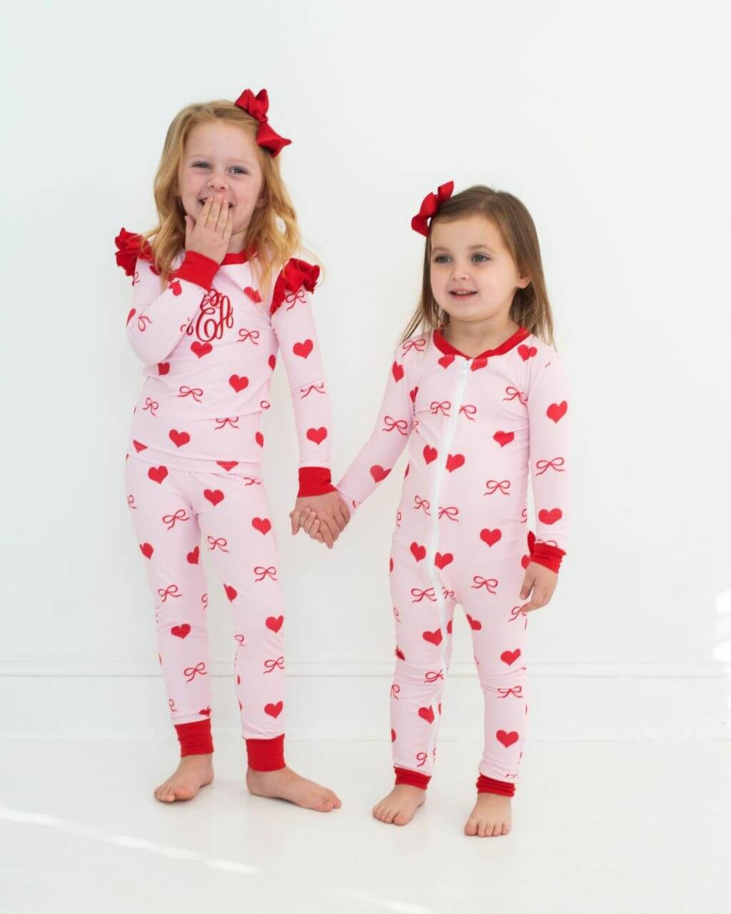Two children wearing pink pajamas with red hearts and bows on a white background