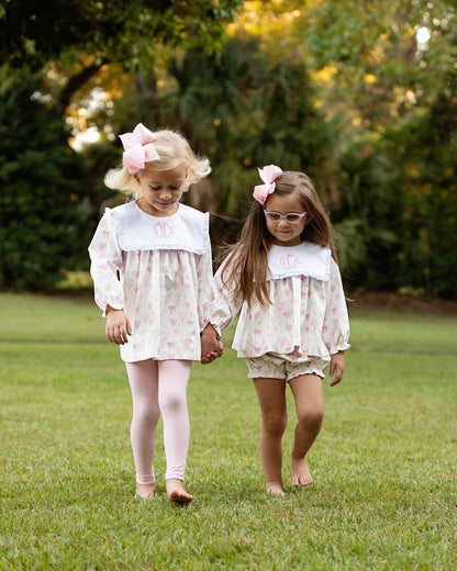 Two girls in matching outfits walking on grass with trees in the background